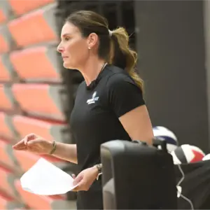 Side profile of Cathy Helin reviewing notes near volleyball equipment, showcasing coaching and athlete development strategies.