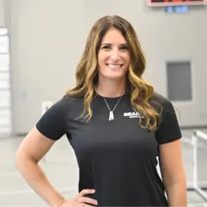 Cathy smiles at camera in gym wearing a Bearcat Coaching polo, showing expertise in athlete training.