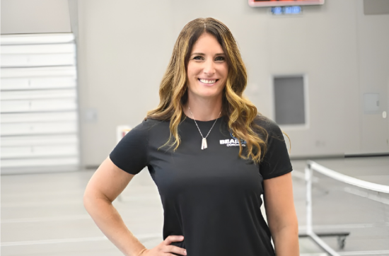 Cathy smiles at camera in gym wearing a Bearcat Coaching polo, showing expertise in athlete training.