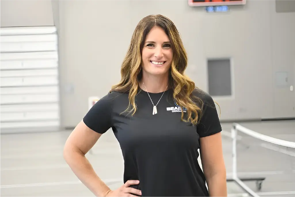 Cathy smiles at camera in gym wearing a Bearcat Coaching polo, showing expertise in athlete training.