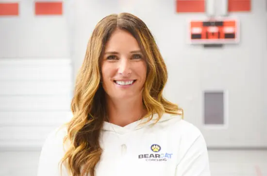 Cathy Helin in a white polo indoors, confident representing mindset coaching for athletes, parents, and coaches.
