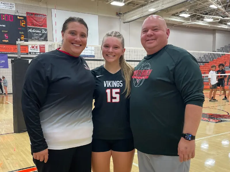 Cathy Helin poses with volleyball players and staff in the gym, symbolizing mentorship and mindset coaching.