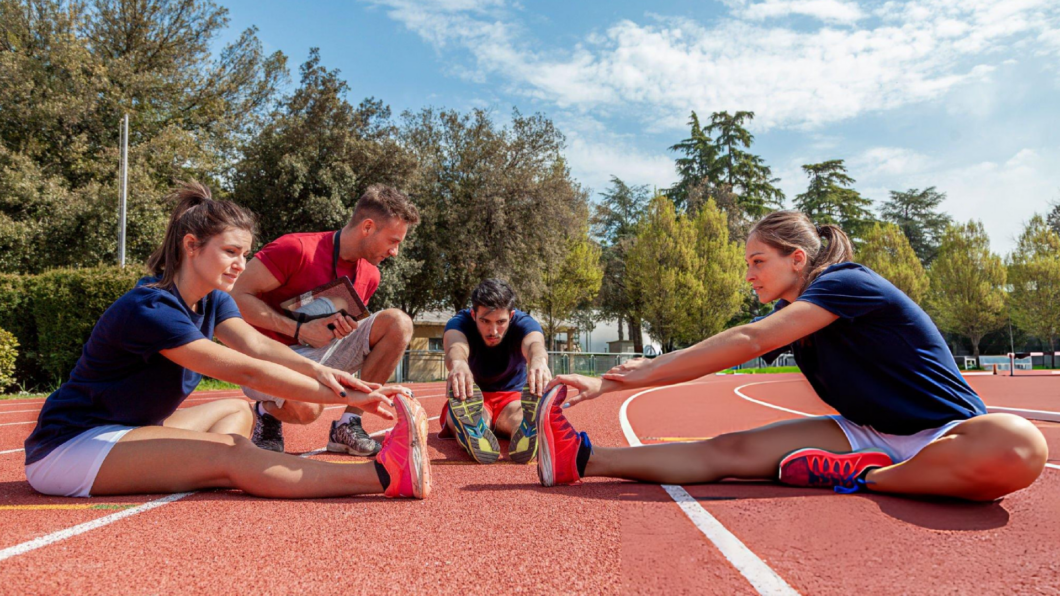 Athletics coach supervising stretching exercises on running track, improving flexibility, performance, injury prevention, and athlete preparation daily.
