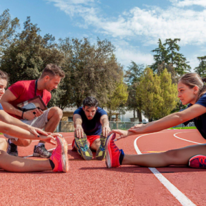 Athletics coach supervising stretching exercises on running track, improving flexibility, performance, injury prevention, and athlete preparation daily.