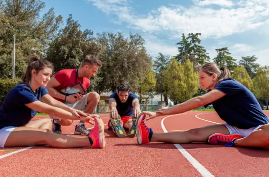 Athletics coach supervising stretching exercises on running track, improving flexibility, performance, injury prevention, and athlete preparation daily.