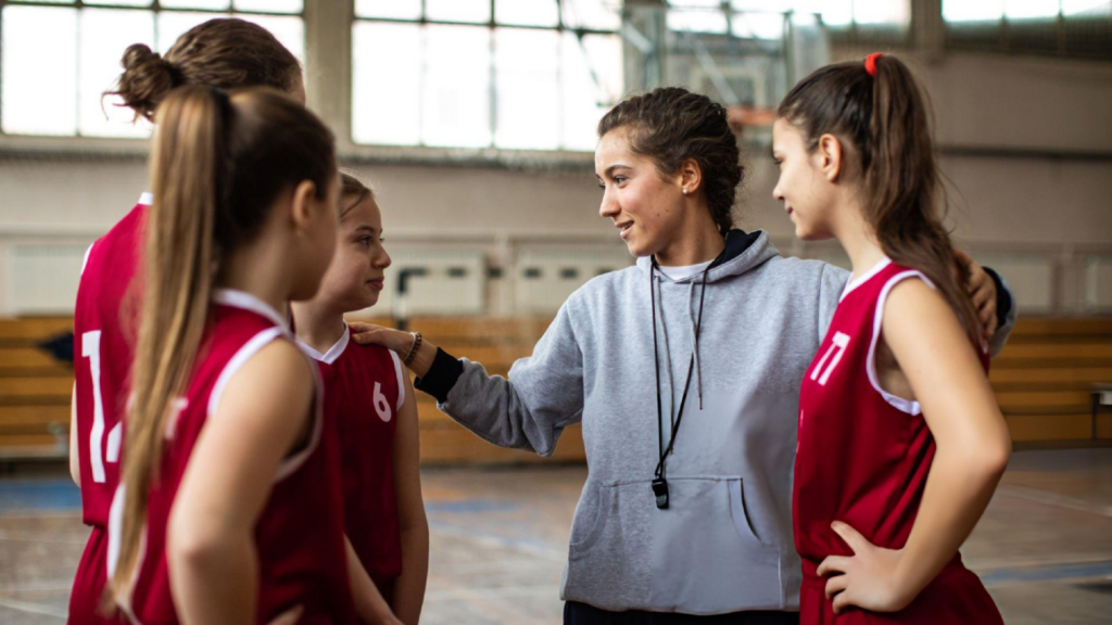 Basketball coach encouraging young players during practice, fostering teamwork, confidence, discipline, motivation, and positive sportsmanship every session.