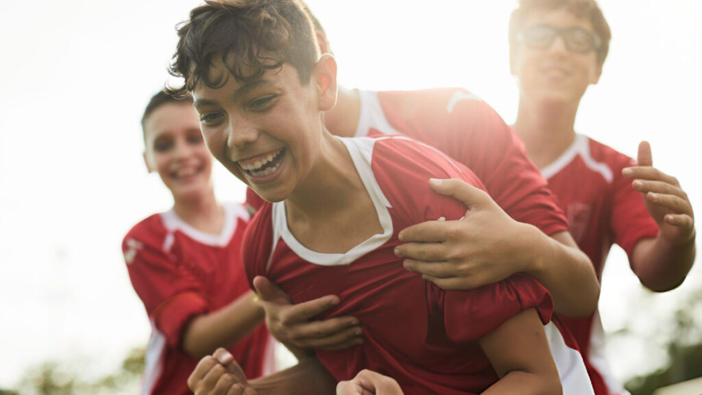 Young soccer teammates celebrating victory together with smiles, teamwork, confidence, energy, friendship, and shared success on field.