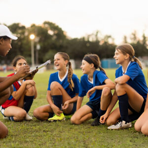 Youth soccer coach leading a team discussion with young female players during outdoor leadership training before practice session.