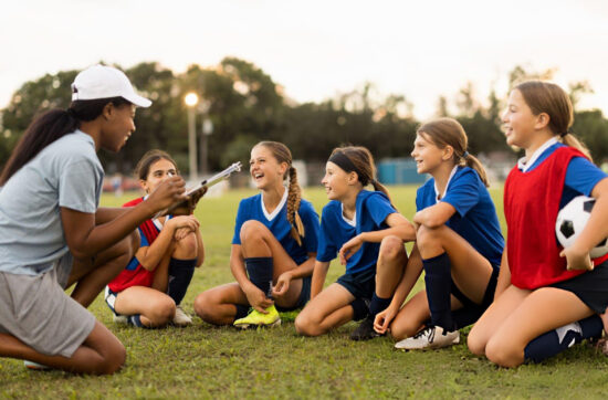 Youth soccer coach leading a team discussion with young female players during outdoor leadership training before practice session.