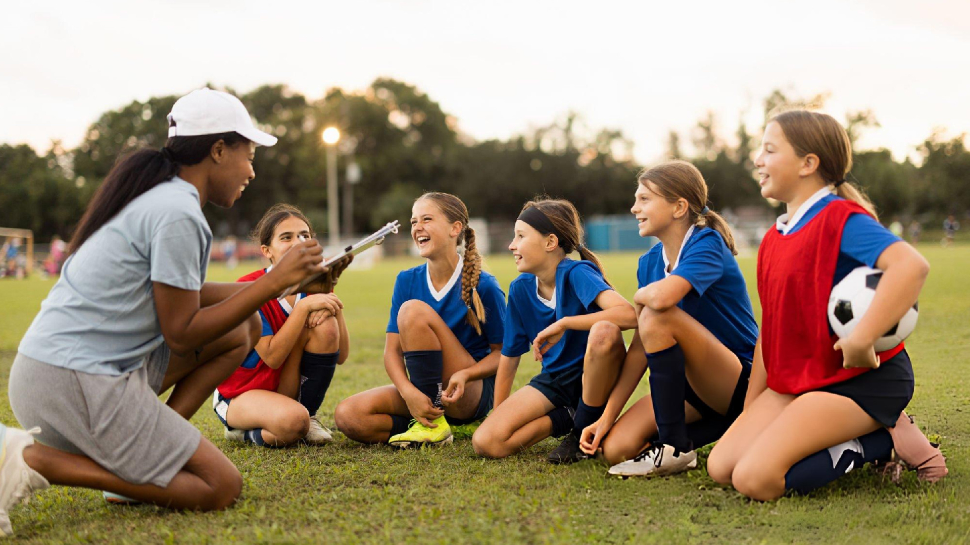 Youth soccer coach leading a team discussion with young female players during outdoor leadership training before practice session.