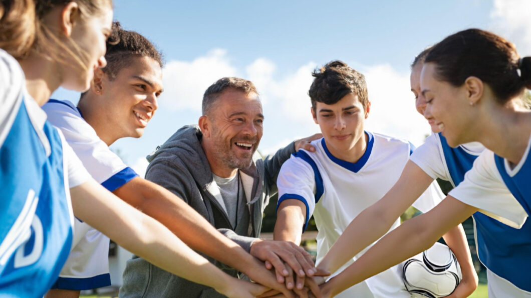 Sport coach motivating young athletes during team huddle, building leadership, communication, confidence, teamwork, and winning mindset together.
