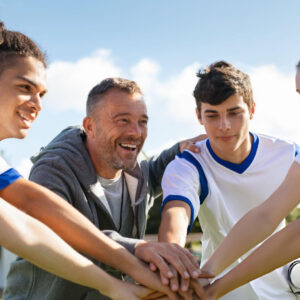 Sport coach motivating young athletes during team huddle, building leadership, communication, confidence, teamwork, and winning mindset together.