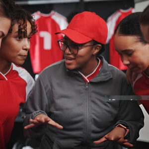 Coach discussing strategy with four young female athletes in red uniforms during a team training session.
