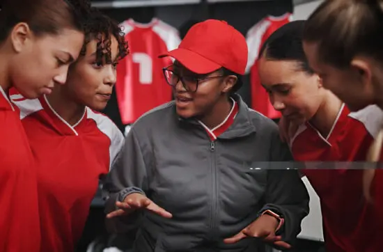 Coach discussing strategy with four young female athletes in red uniforms during a team training session.