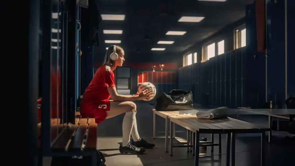 Female volleyball player preparing in a locker room, holding a volleyball while getting ready for competition.