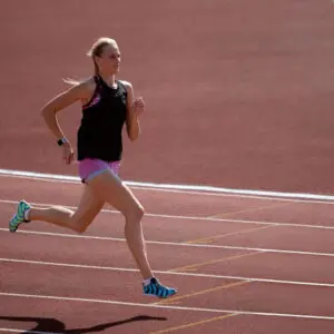 Female athlete running on a track during outdoor training, demonstrating speed, strength, focus, and athletic determination.