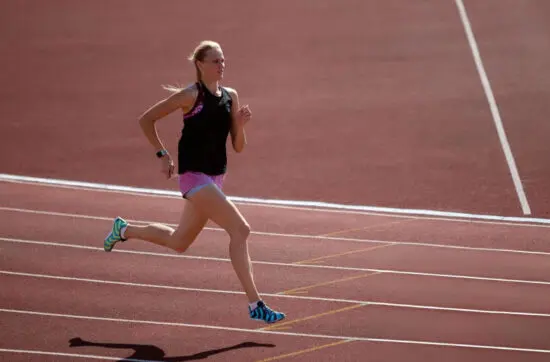 Female athlete running on a track during outdoor training, demonstrating speed, strength, focus, and athletic determination.
