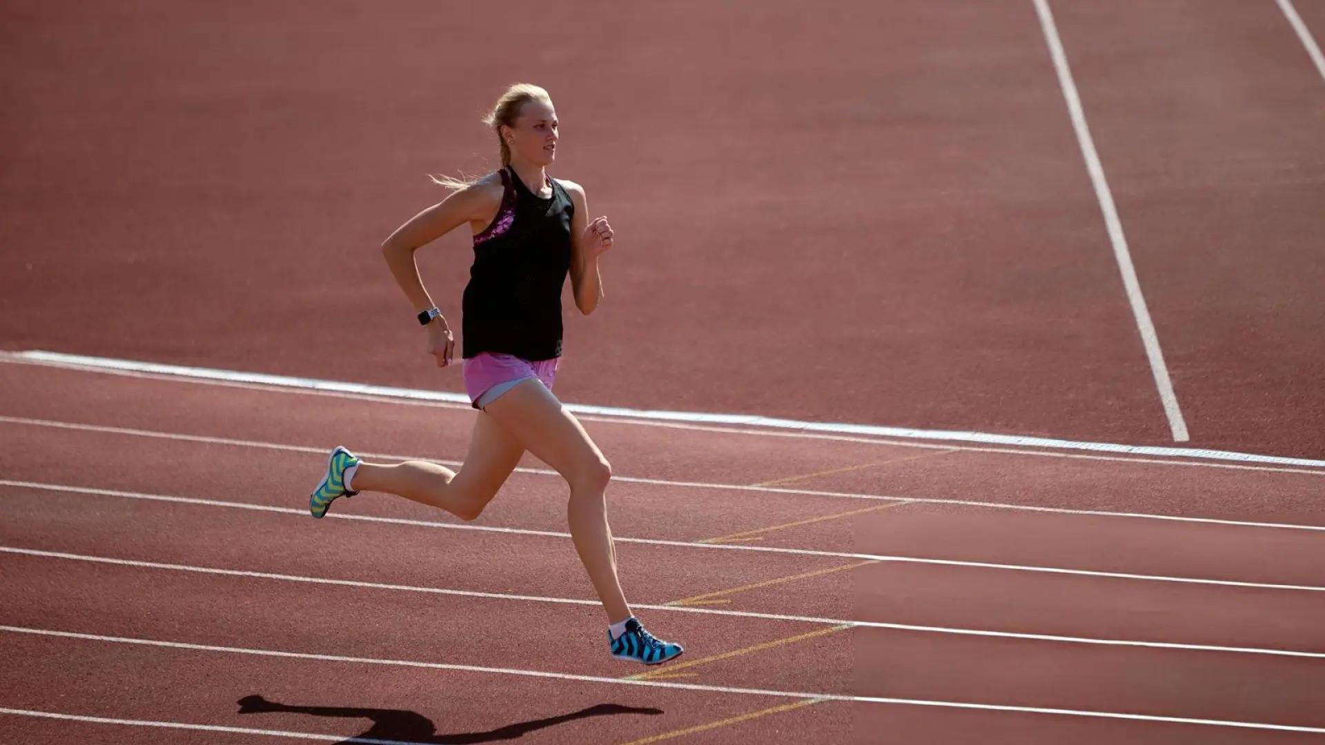 Female athlete running on a track during outdoor training, demonstrating speed, strength, focus, and athletic determination.
